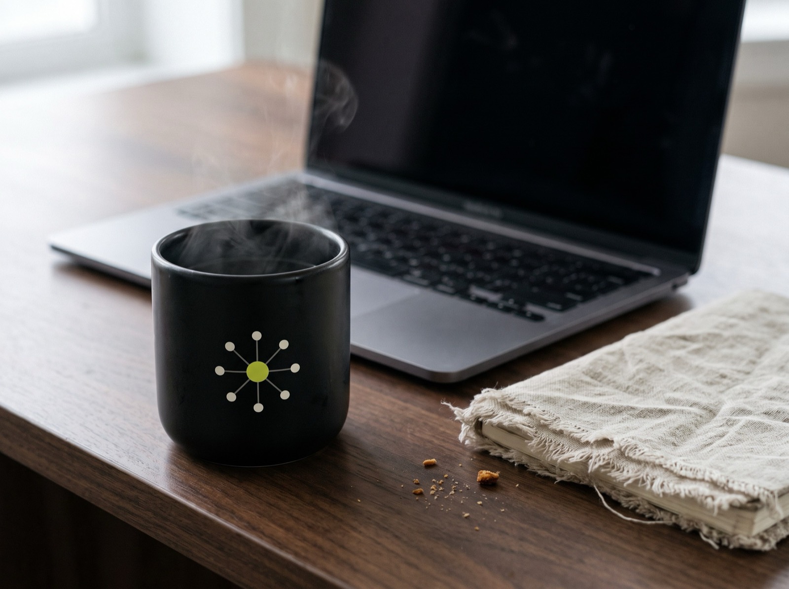 A steaming IAW mug beside a laptop on a wooden desk — brand visual
