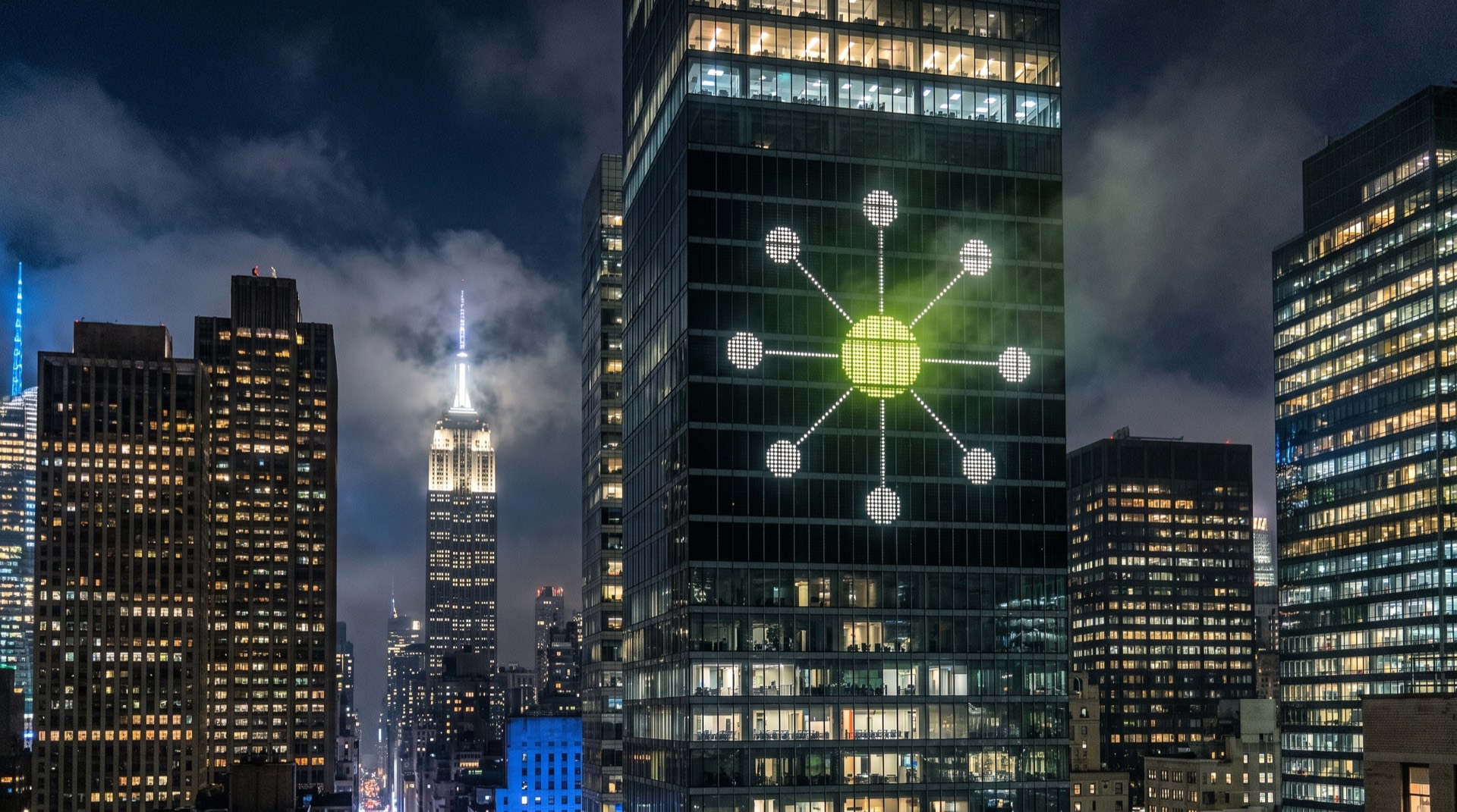 The IAW hub mark glowing on a night-lit skyline — brand visual